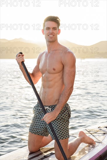 Caucasian man kneeling on paddleboard in river