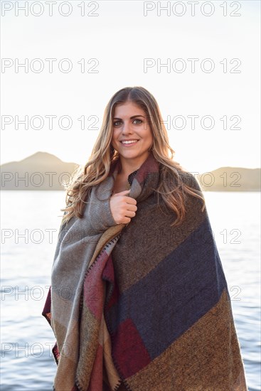 Hispanic woman wrapped in blanket at river