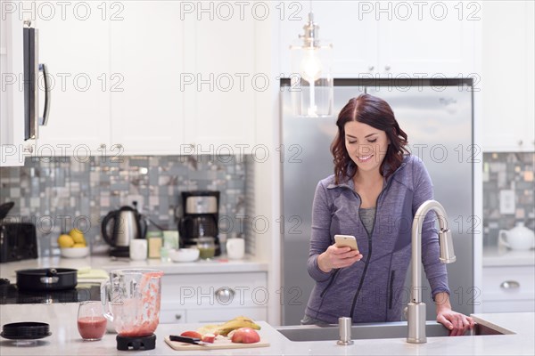 Caucasian woman texting on cell phone in domestic kitchen
