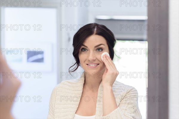 Caucasian woman cleaning face with pad in mirror