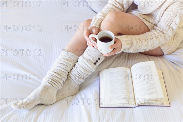 Caucasian woman reading book on bed and drinking coffee