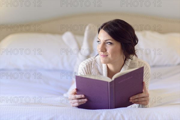 Pensive Caucasian woman laying on bed reading book