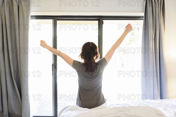 Caucasian woman sitting on bed stretching arms