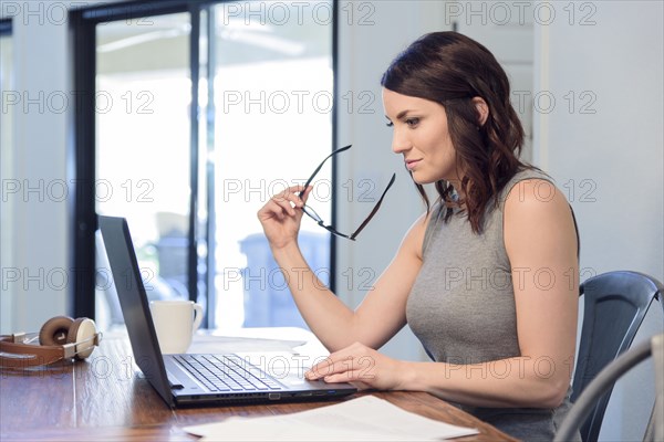 Pensive Caucasian woman holding eyeglasses using laptop