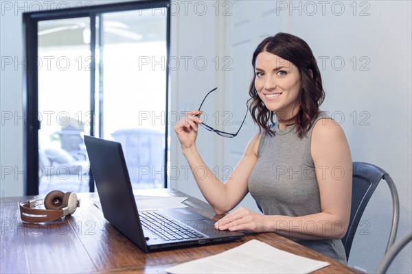 Smiling Caucasian woman holding eyeglasses using laptop