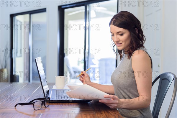 Caucasian woman reading paperwork and using laptop
