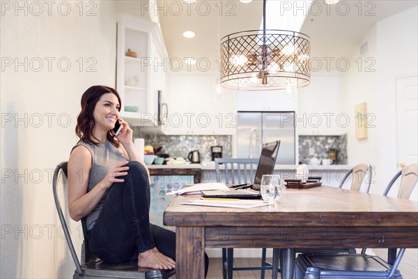 Caucasian woman sitting at table near laptop talking on cell phone