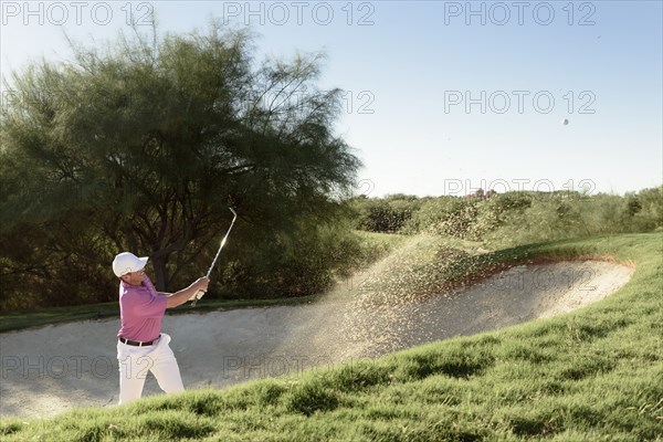 Hispanic golfer hitting ball in sand trap