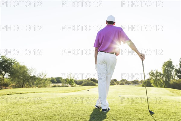 Hispanic golfer leaning on golf club on golf course