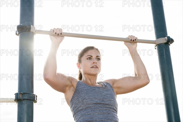 Hispanic woman doing chin-up outdoors