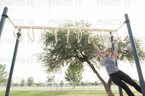 Hispanic woman swinging on monkey bars outdoors