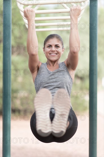 Hispanic woman hanging on monkey bars outdoors