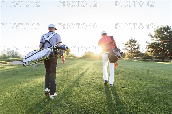 Men carrying golf bags on sunny golf course