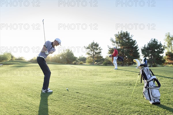 Friend watching man hitting ball on golf course