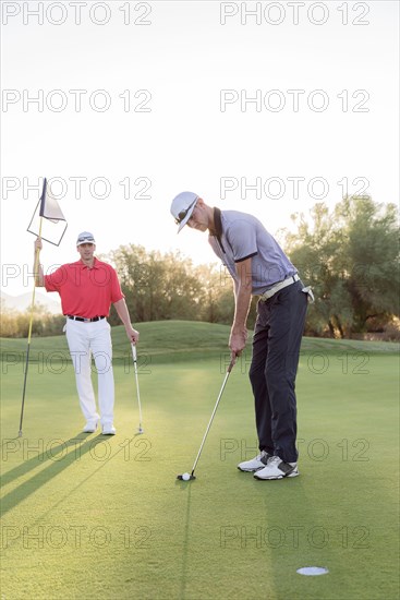 Hispanic man watching friend on golf course