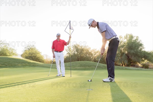Hispanic man watching friend on golf course