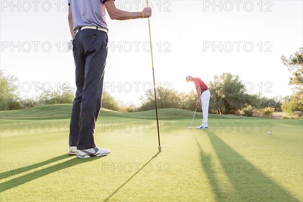 Hispanic man watching friend on golf course