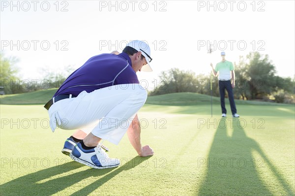 Hispanic man watching friend crouching on golf course
