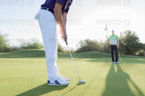 Hispanic man watching friend putting on golf course