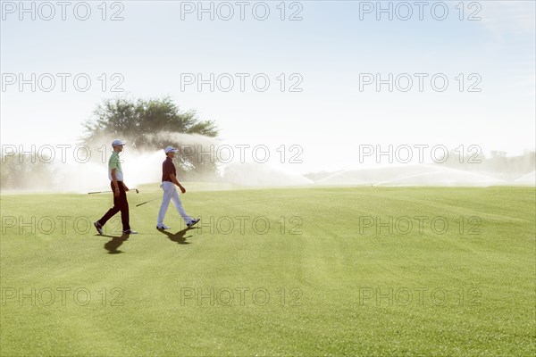Friends walking on golf course near sprinklers