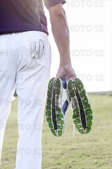 Hispanic man hold golf shoes covered with grass