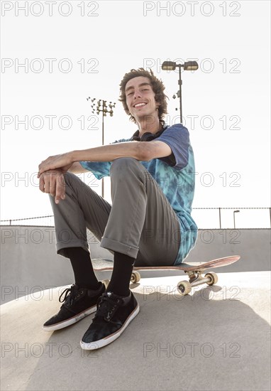 Portrait of smiling Hispanic man sitting on skateboard