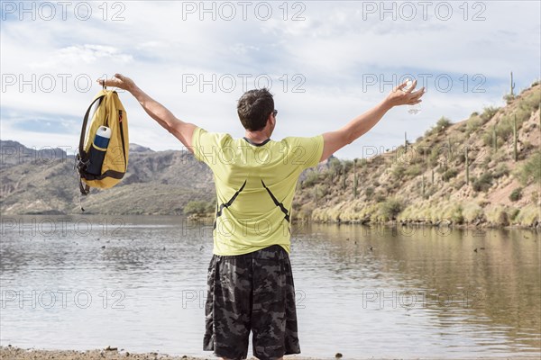 Hispanic man celebrating with arms raised at lake