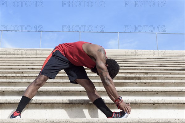 African American man stretching leg on bleachers