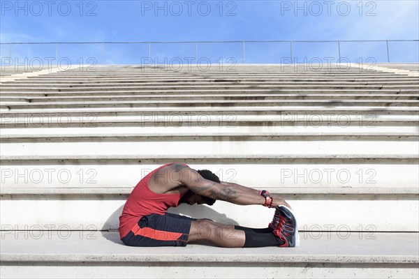 African American man stretching legs on bleachers