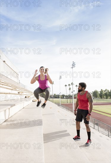 Trainer watching woman jumping on bleachers