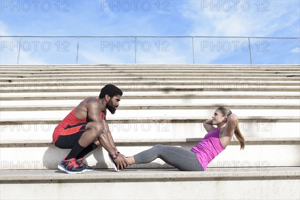 Man holding feet of woman doing sit-ups on bleachers