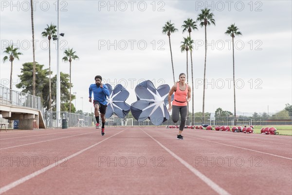 Man and woman running with parachutes on track