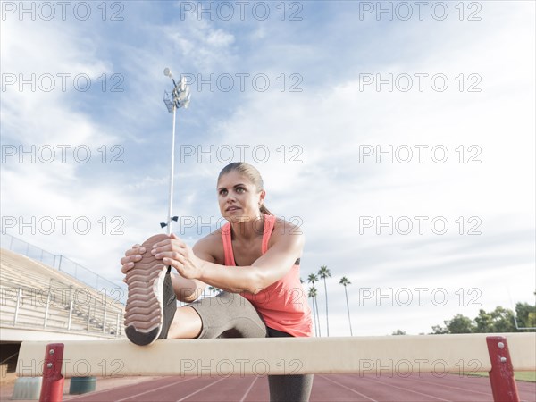 Hispanic woman stretching leg on hurdle