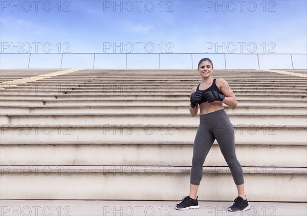 Hispanic woman wearing boxing gloves standing on bleachers