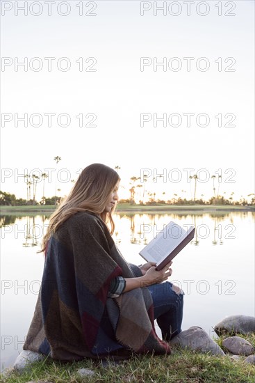 Hispanic woman sitting bear lake reading book