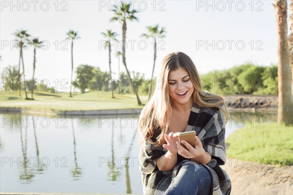 Hispanic woman texting on cell phone near pond