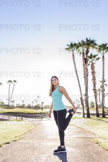 Hispanic woman stretching leg on path