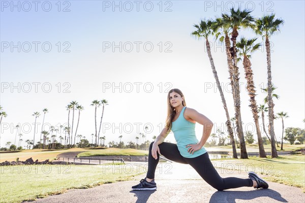 Hispanic woman kneeling and stretching on path