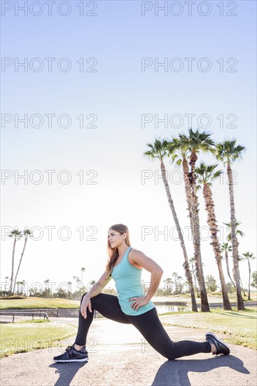 Hispanic woman kneeling and stretching on path