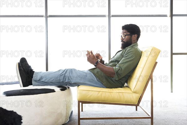 Black man sitting in chair texting on cell phone