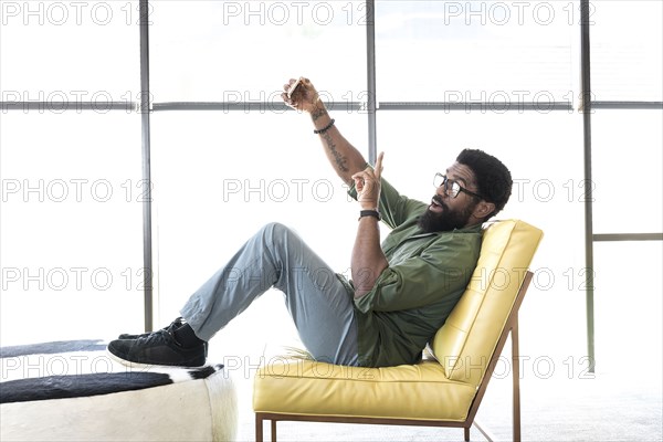 Black man sitting in chair posing for cell phone selfie