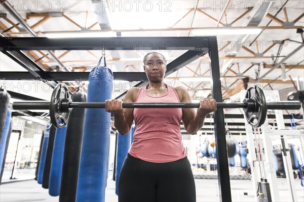 Black woman lifting barbell in gymnasium