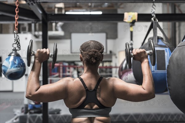 Black woman lifting dumbbells in gymnasium