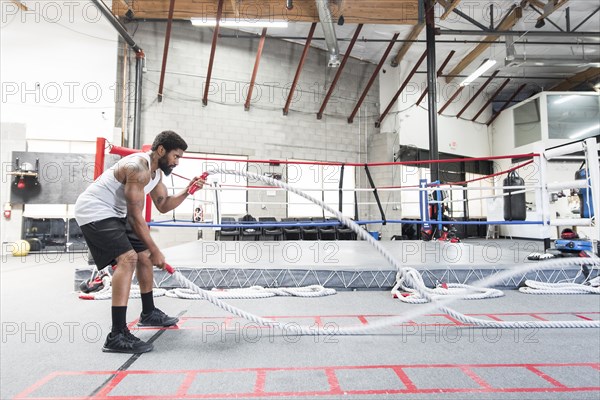 Black man lifting heavy ropes in gymnasium