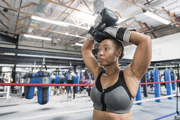Black woman resting with arms raised in boxing ring