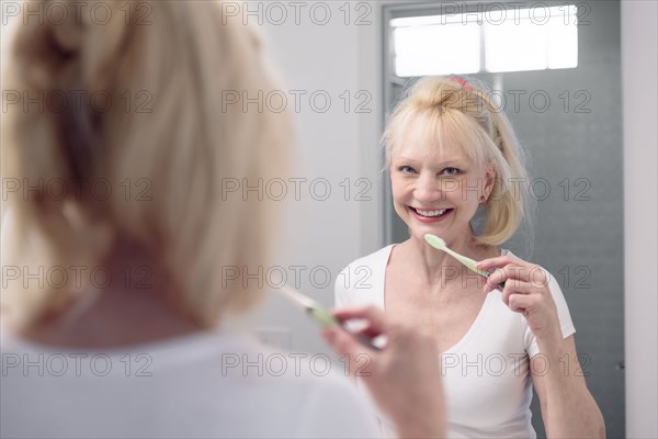 Caucasian woman brushing teeth in mirror
