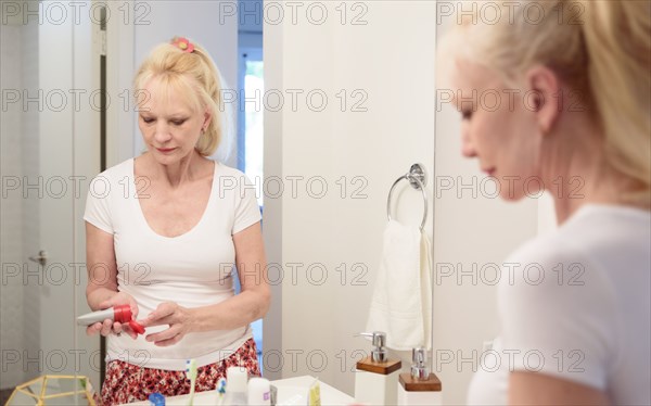 Caucasian woman squeezing lotion onto finger in mirror