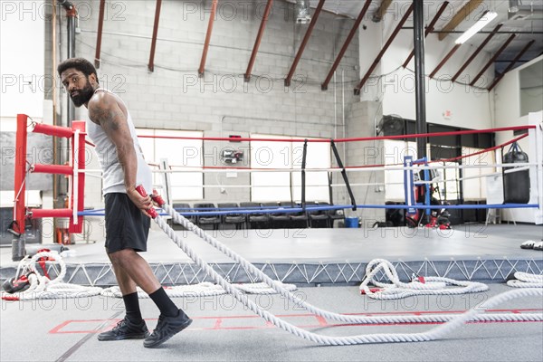 Black man pulling heavy ropes in gymnasium