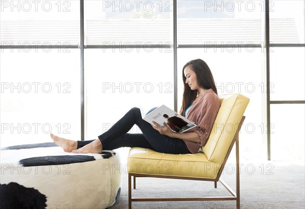 Mixed race woman sitting on chair reading book