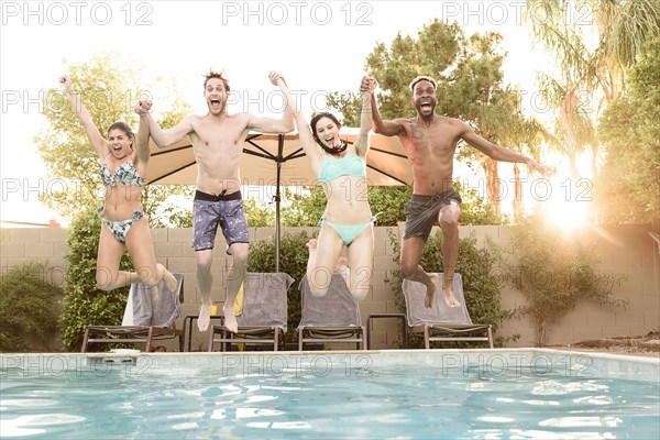 Friends holding hands jumping into swimming pool